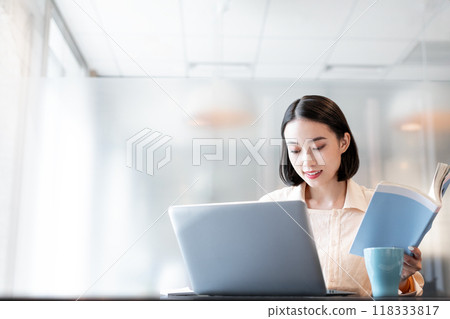 A woman operating a computer with a book in one hand A woman operating a computer with a book in one hand 118333817