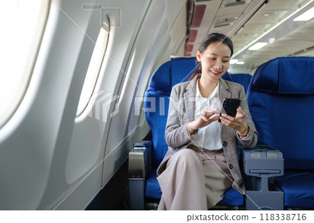 A woman is sitting on an airplane and looking at her cell phone A woman is sitting on an airplane and looking at her cell phone 118338716