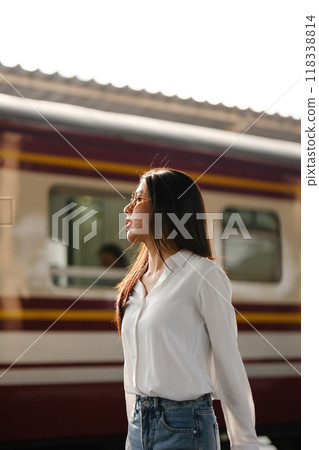 A woman stands in front of a train, wearing a white shirt and blue jeans A woman stands in front of a train, wearing a white shirt and blue jeans 118338814