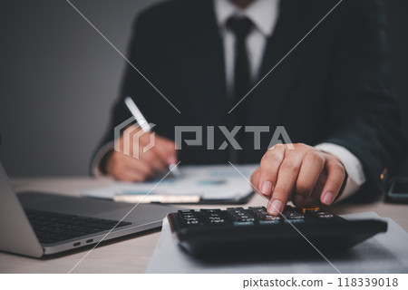 Close-up of a businessman in a suit working at a desk. Hand pressing calculator, analyzing documents. Professional, focused on financial calculations. Suitable for business, finance, Close-up of a businessman in a suit working at a desk. Hand pressing calculator, analyzing documents. Professional, focused on financial calculations. Suitable for business, finance, 118339018