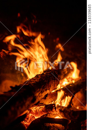 The glow of a campfire casts flickering light on logs, creating a cozy atmosphere under the night sky. The glow of a campfire casts flickering light on logs, creating a cozy atmosphere under the night sky. 118339685