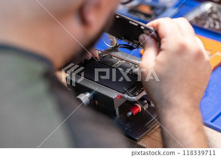 A skilled technician carefully replaces a phone battery in a repair workshop, focusing on precision and detail. 118339711