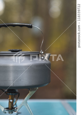 A kettle is heating up on a small camping stove as steam begins to rise in the cool forest air. A kettle is heating up on a small camping stove as steam begins to rise in the cool forest air. 118339722