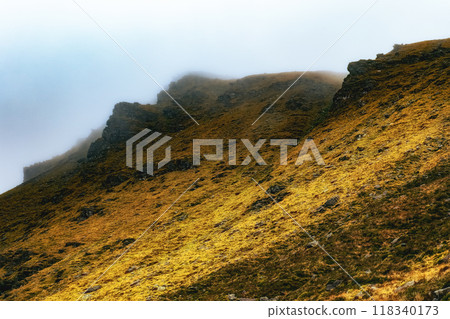 Misty mountain landscape with golden grass and rocky outcrops in foggy conditions during early morning hours. Misty mountain landscape with golden grass and rocky outcrops in foggy conditions during early morning hours. 118340173