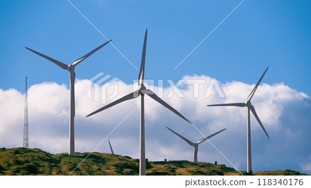 A row of wind turbines are located on a hill, against a backdrop of a cloudy sky. A row of wind turbines are located on a hill, against a backdrop of a cloudy sky. 118340176