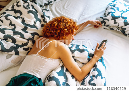portrait of red-haired young woman lying on bed using mobile phone portrait of red-haired young woman lying on bed using mobile phone 118340329