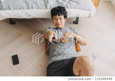 Man lying on the floor eating snack and watching TV on the weekends. 118340449