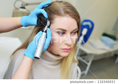 A dermatologist holds a dermatoscope in his hands and examines the structure of a young woman's hair. Trichoscopy is the science of hair structure. 118340831