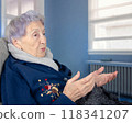Elderly Alzheimer's patient in a nursing home setting, gesturing while talking to herself, highlighting the effects of senile dementia on communication and cognitive decline. 118341207