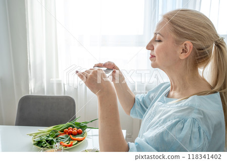 A woman is holding a smartphone and capturing a photo of a nutritious breakfast spread A woman is holding a smartphone and capturing a photo of a nutritious breakfast spread 118341402