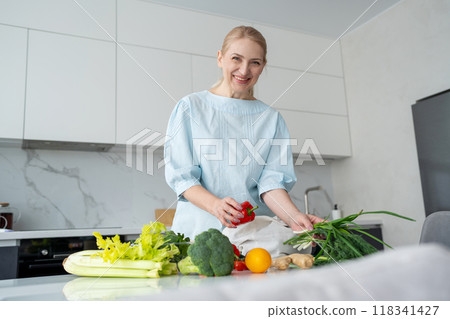 A happy woman is seen holding orange and red bell peppers in a modern kitchen setting A happy woman is seen holding orange and red bell peppers in a modern kitchen setting 118341427