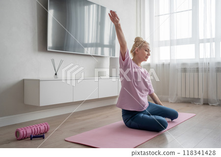 Practicing yoga, a woman is in her cozy living room, surrounded by calm energy and natural light Practicing yoga, a woman is in her cozy living room, surrounded by calm energy and natural light 118341428