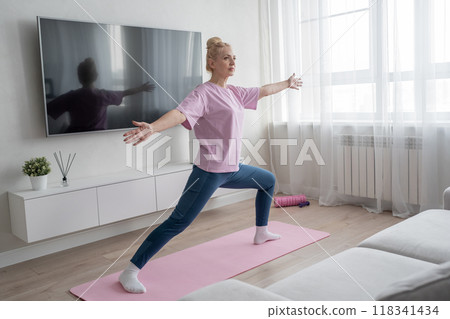 Practicing yoga, a woman is in her cozy living room, surrounded by calm energy and natural light 118341434
