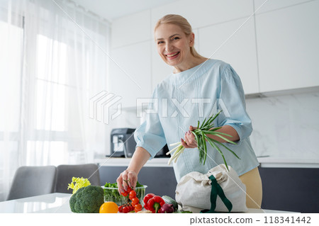 A happy woman is seen holding orange and red bell peppers in a modern kitchen setting A happy woman is seen holding orange and red bell peppers in a modern kitchen setting 118341442
