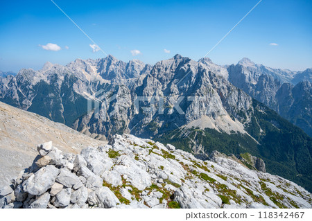 Breathtaking vistas of the Julian Alps stretch out, showcasing the rugged beauty of Skrlatica, Prisank, Razor, and Triglav Mountains under a clear blue sky. 118342467