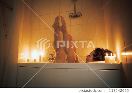 A woman is in a bathtub with candles lit around her. She is barefoot and has her legs up in the air. A woman is in a bathtub with candles lit around her. She is barefoot and has her legs up in the air. 118342623