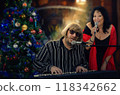 Christmas party comes alive with music - pianist and singer perform by brightly lit holiday tree. 118342662