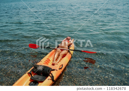 A woman is laying on a kayak in the water. The kayak is orange and has a paddle on it. The woman is wearing a red hat. 118342678