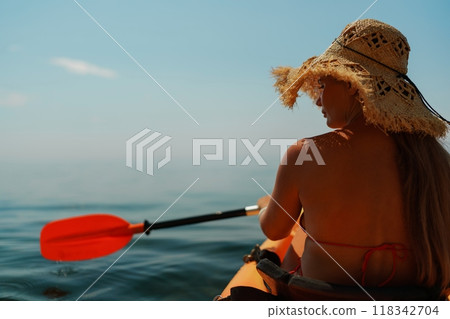 Woman in kayak back view. Happy woman with long hair in a swimsuit and hat floating in kayak on the sea. Summer holiday vacation. Summer holidays vacation at sea. 118342704