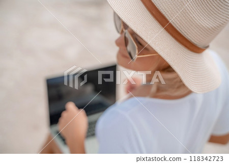 Freelance women sea working on the computer. Good looking middle aged woman typing on a laptop keyboard outdoors with a beautiful sea view. The concept of remote work. Freelance women sea working on the computer. Good looking middle aged woman typing on a laptop keyboard outdoors with a beautiful sea view. The concept of remote work. 118342723