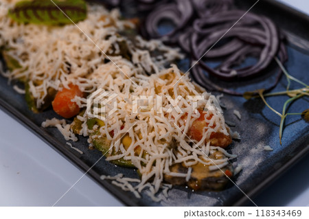 Gourmet Plated Dish of Baked Vegetables Topped with Grated Cheese on Elegant Dark Ceramic Platter 118343469
