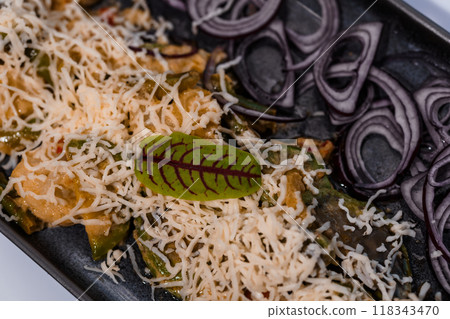Freshly Shredded Cheese and Red Onion Garnished Savory Delicacy with Herb Leaf in Elegant Presentation on Dark Plate 118343470