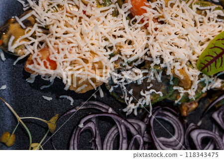 Exquisite Close-Up of a Flavorful Vegetable Dish with Grated Cheese Topping and Purple Onion Garnish on Dark Plate Exquisite Close-Up of a Flavorful Vegetable Dish with Grated Cheese Topping and Purple Onion Garnish on Dark Plate 118343475