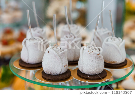 Elegant Frosted Rose-Shaped Desserts with Silver Spoons Displayed on Glass Stand at Gourmet Event Elegant Frosted Rose-Shaped Desserts with Silver Spoons Displayed on Glass Stand at Gourmet Event 118343507