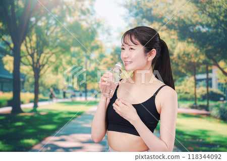 年輕女子在外面跑步時喝水 年輕女子在外面跑步時喝水 118344092