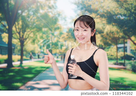 Young woman drinking water while running outside 118344102