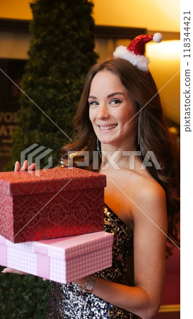 Girl holding Christmas present near New Year tree. Happiness emotions 118344421