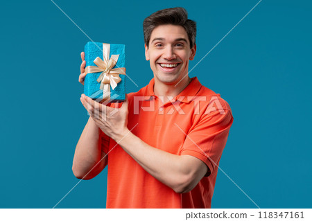 Handsome Man Holding Gift Box And Gives It By Hands To Camera on Blue 118347161