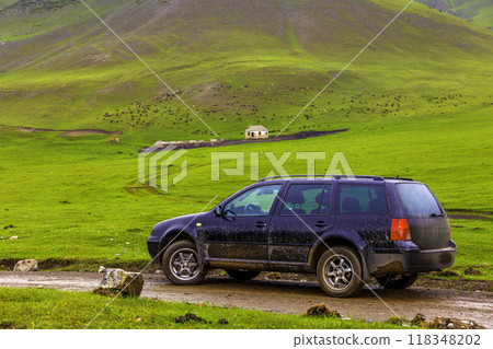 black car on a side of wet dirt road in the mountain hills in front of sheep grazing on green pasture at rainy day near farm ruins black car on a side of wet dirt road in the mountain hills in front of sheep grazing on green pasture at rainy day near farm ruins 118348202
