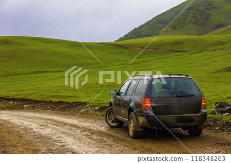 black car on a side of wet dirt road in the mountain hills at rainy summer day 118348203