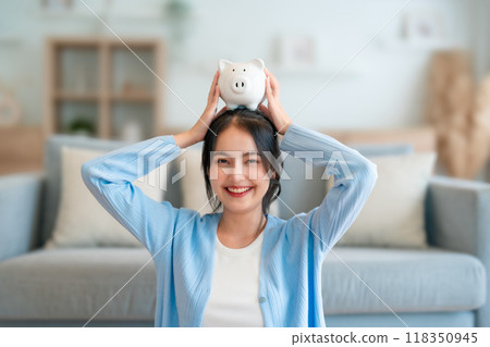 Young Asian woman holding piggy bank and sitting on the floor at home 118350945