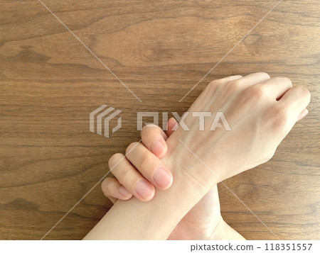 A woman's hand holding her wrist on a desk A woman's hand holding her wrist on a desk 118351557
