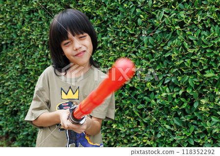 Smiling asian boy playing plastic red lightsaber sword toy at the playground. Outdoor childhood play and imagination concept. Smiling asian boy playing plastic red lightsaber sword toy at the playground. Outdoor childhood play and imagination concept. 118352292