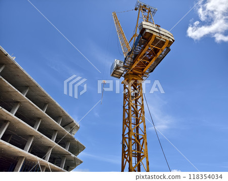 A large yellow crane stands out against a bright blue sky 118354034