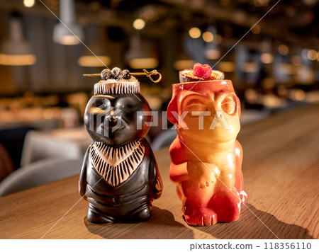 Authentic Tiki Drink Cocktails. Two tropical tiki cocktails on bar counter. Tiki cocktails on bar in night club or restaurant interior Authentic Tiki Drink Cocktails. Two tropical tiki cocktails on bar counter. Tiki cocktails on bar in night club or restaurant interior 118356110