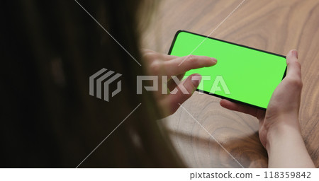 Young woman sitting at a table and using a smartphone with horizontal green screen Young woman sitting at a table and using a smartphone with horizontal green screen 118359842