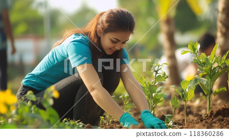 A group of young volunteers working together in a community gardening project. Focus on a smiling girl with gloves. Outdoor setting, teamwork, and environmental care concept 118360286