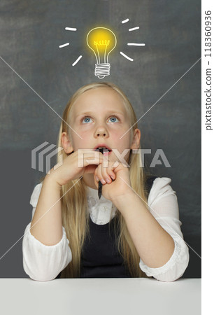 Clever child girl student with yellow light bulb on school blackboard background. 118360936
