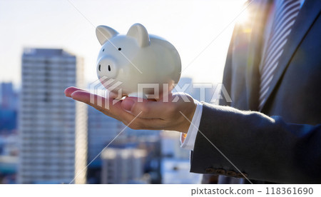 A man in a suit holding a piggy bank in his hand. Image of savings or deposit amount. City skyscrapers background. 118361690
