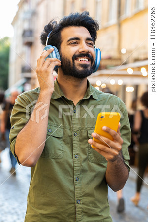 Happy young man in wireless headphones choosing, listening music dancing outdoors city street Happy young man in wireless headphones choosing, listening music dancing outdoors city street 118362266
