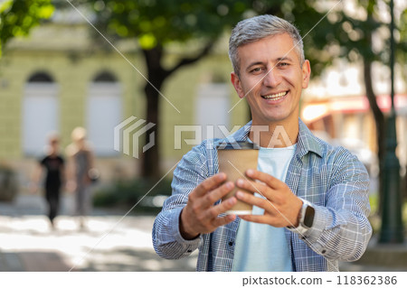 Happy mature Caucasian man enjoying drinking morning coffee hot drink and smiling on city street Happy mature Caucasian man enjoying drinking morning coffee hot drink and smiling on city street 118362386