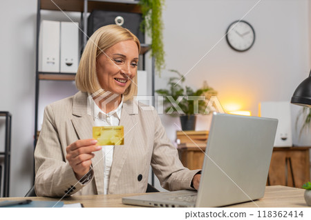 Mature businesswoman using bank credit card and laptop for online shopping payments at home office 118362414
