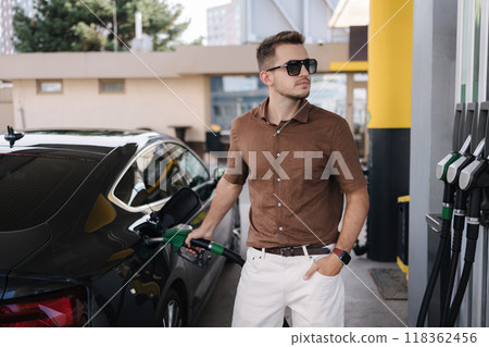 Bearded man in sunglasses refueling car on gas station and looking on fuel pump display. Male looks at the total cost. Luxury car. Fuel price increase 118362456