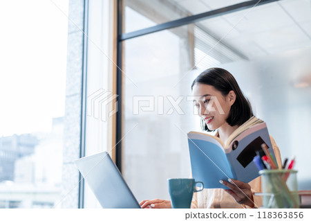 A woman operating a computer with documents in one hand 118363856
