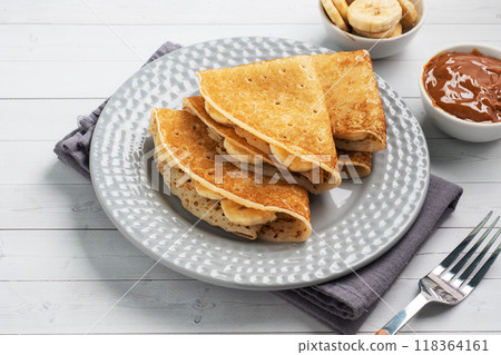 Pancakes with chocolate banana filling. Concept delicious breakfast, a white wooden table. Pancakes with chocolate banana filling. Concept delicious breakfast, a white wooden table. 118364161