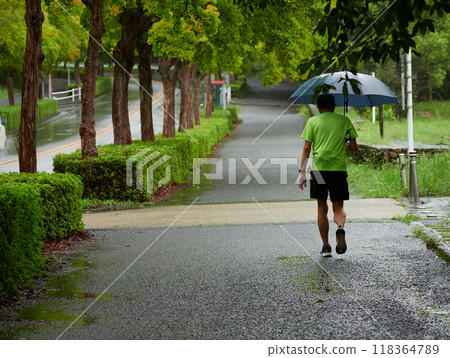 Senior man jogging on the sidewalk of a road on a rainy day Senior man jogging on the sidewalk of a road on a rainy day 118364789